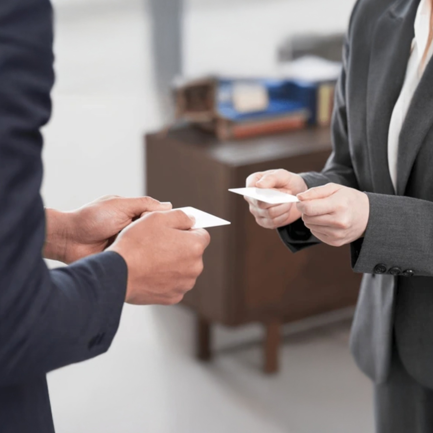Two business professionals exchanging business cards in a formal office setting, symbolizing networking and professional connection.
